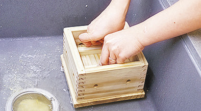豆腐木盒放在一個大深盤中接水， 盒中鋪上豆漿布；並把塊狀豆花倒入豆腐木盒內，豆腐布覆蓋中間，再蓋上木盒蓋。